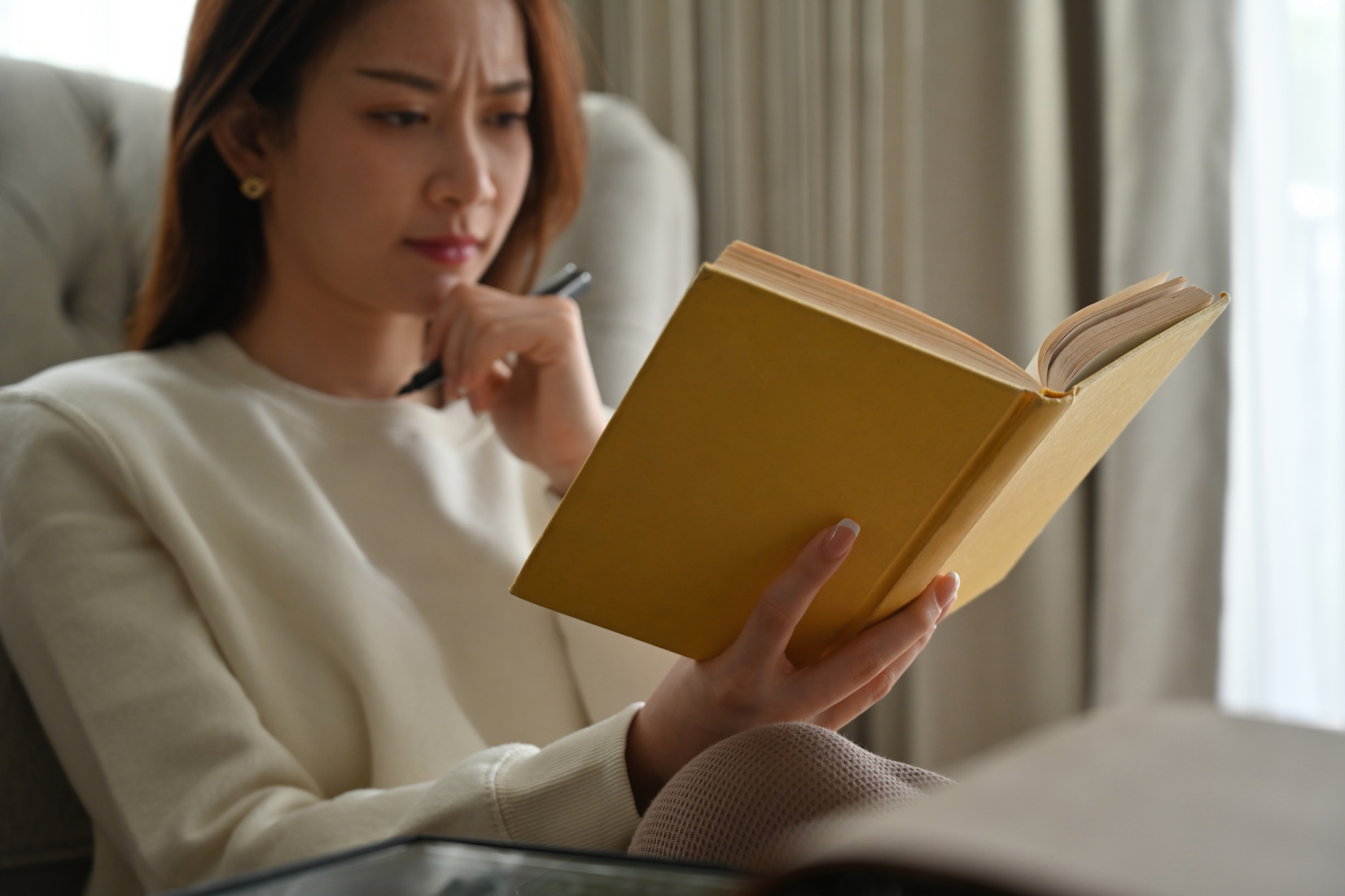 Cropped image of Stressed Asian woman contemplating reading a bo