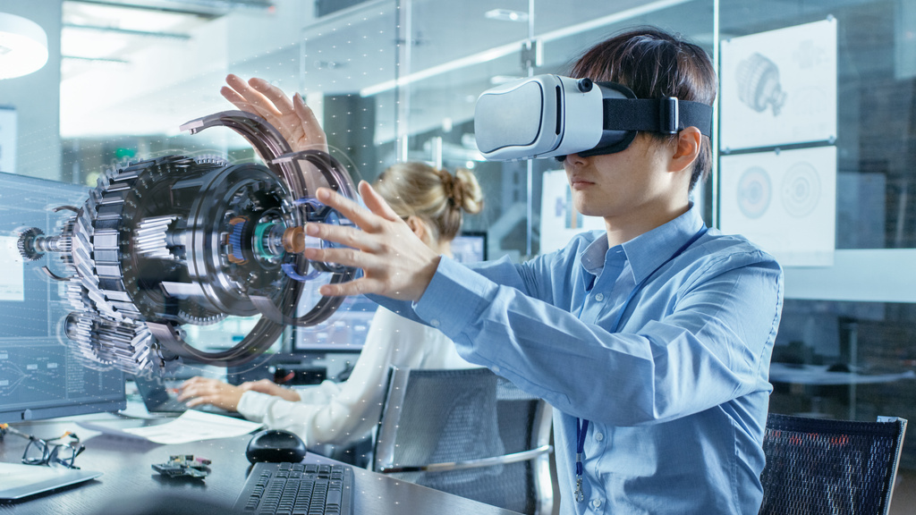 Computer Science Engineer wearing Virtual Reality Headset Works with 3D Model Hologram Visualization, Makes Gestures. In the Background Engineering Bureau with Busy Coworkers.